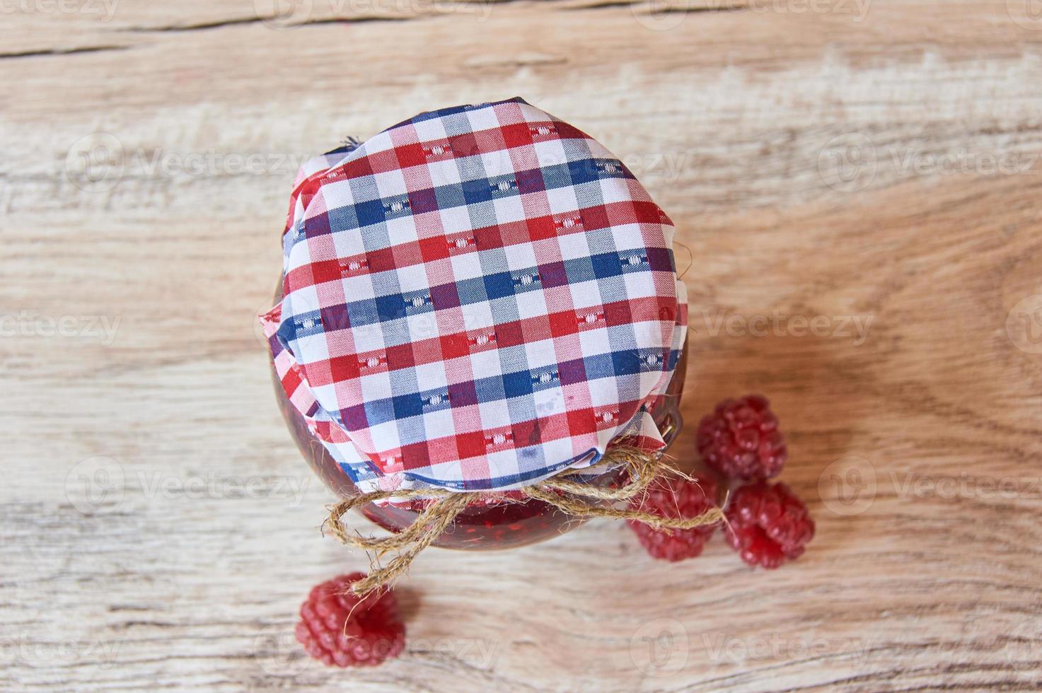 Homemade marmalade. Glass jar with raspberry jam on a wooden background. Preserved berry. Top view. photo