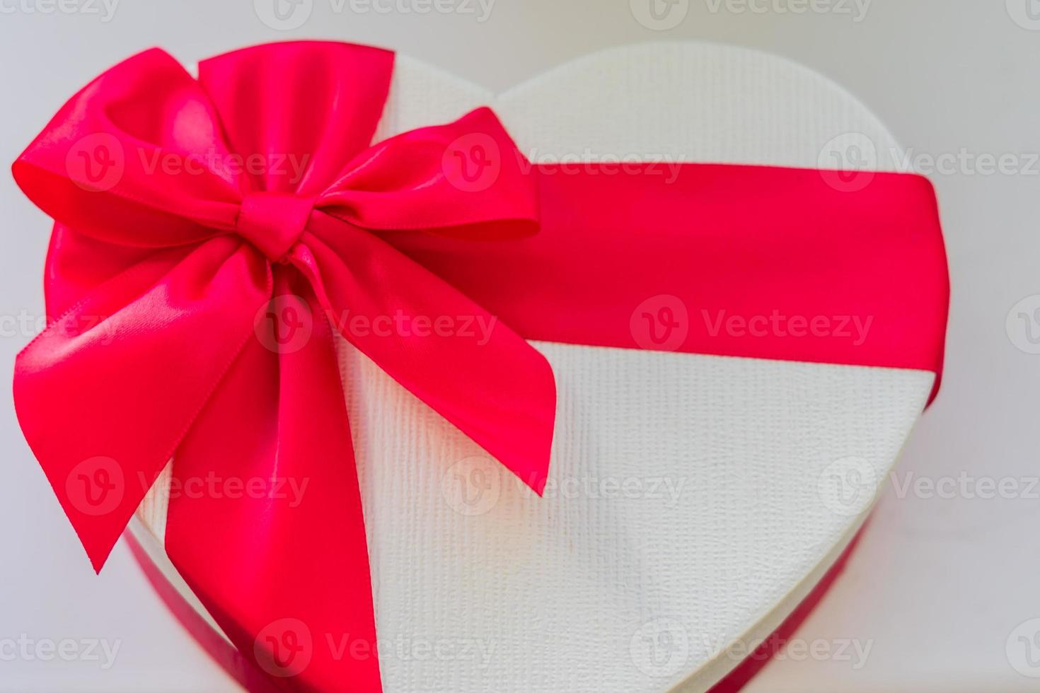 close up of white gift box in a heart shape with red bow and ribbon, top view photo