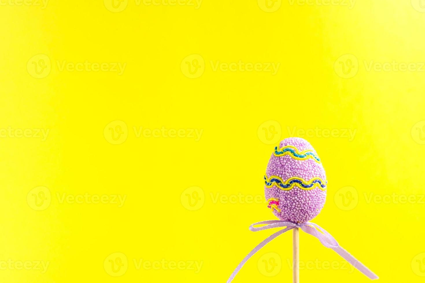 Easter purple decorated egg stand on a wooden stick on yellow background. Minimal easter concept. Happy Easter card with copy space for text. photo