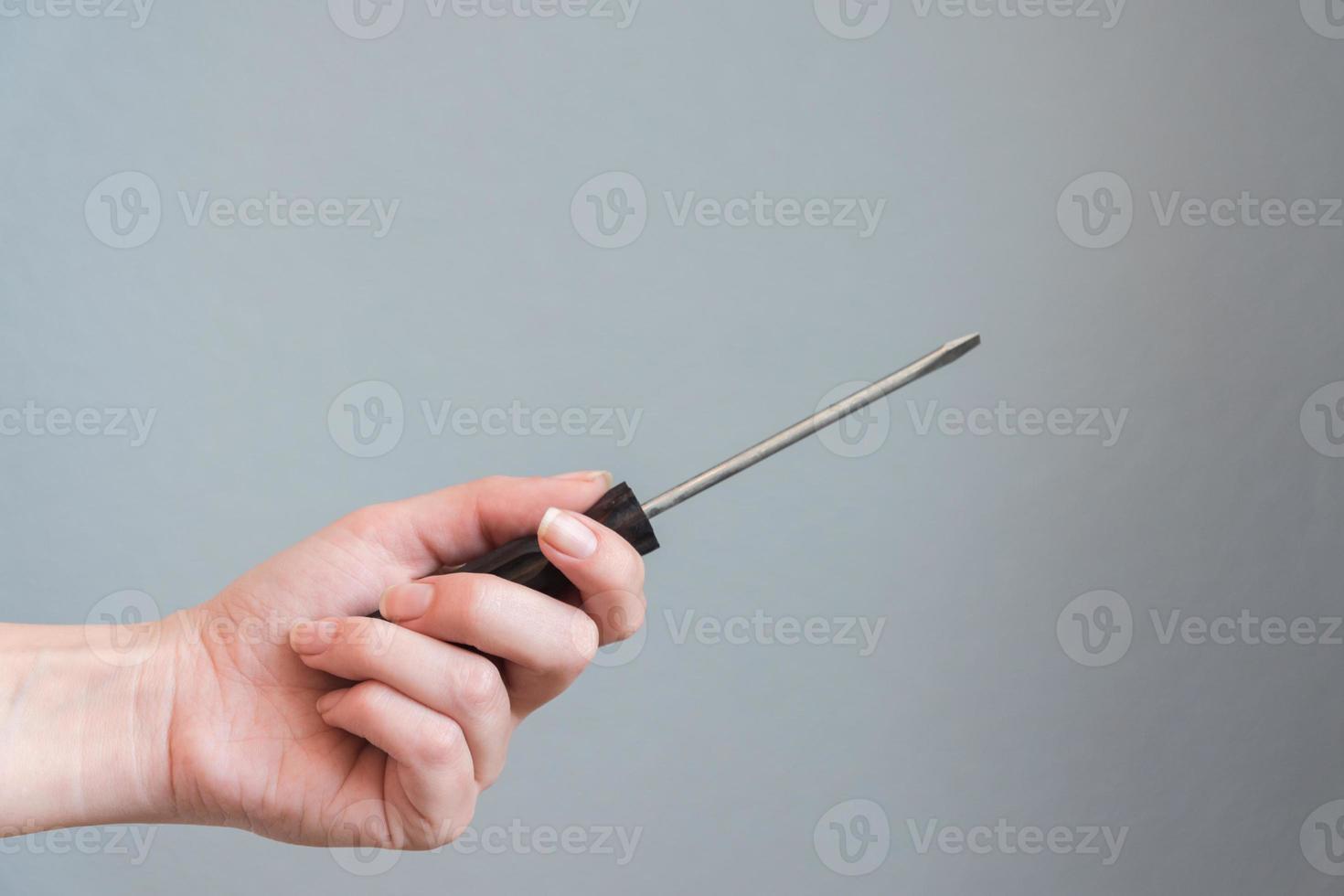 woman holding a screwdriver in her hand on gray background. photo