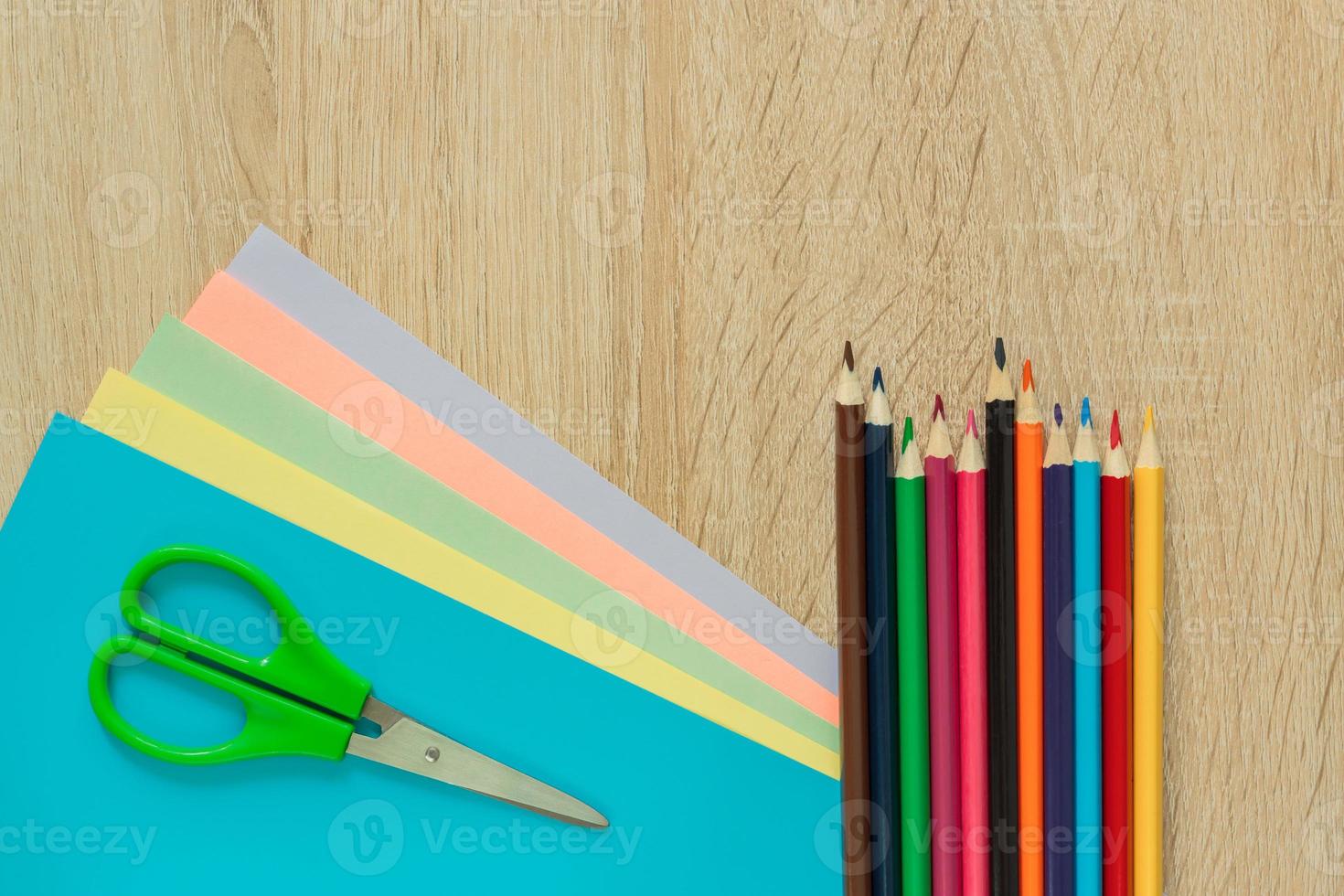 Top view of multicolored paper, pencils and scisors on wooden table. Top view.  Arrangement for creative work or craft. photo