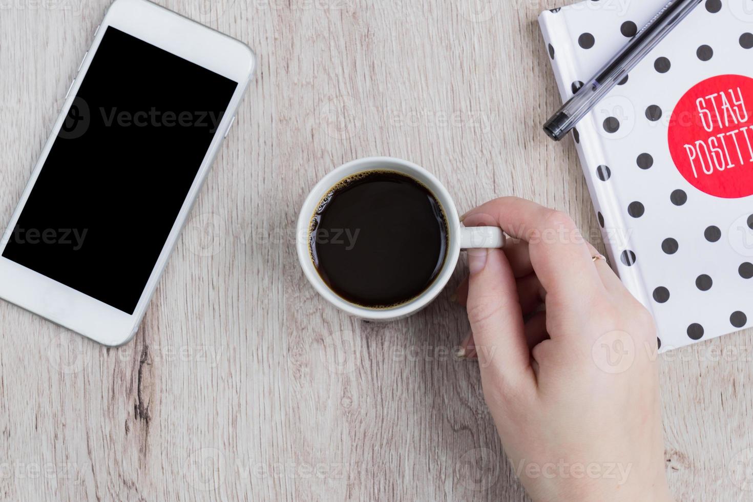 Business and office concept - black and white polka dot cover notebook, smartphone and cup of black coffee on wooden table. top view. photo