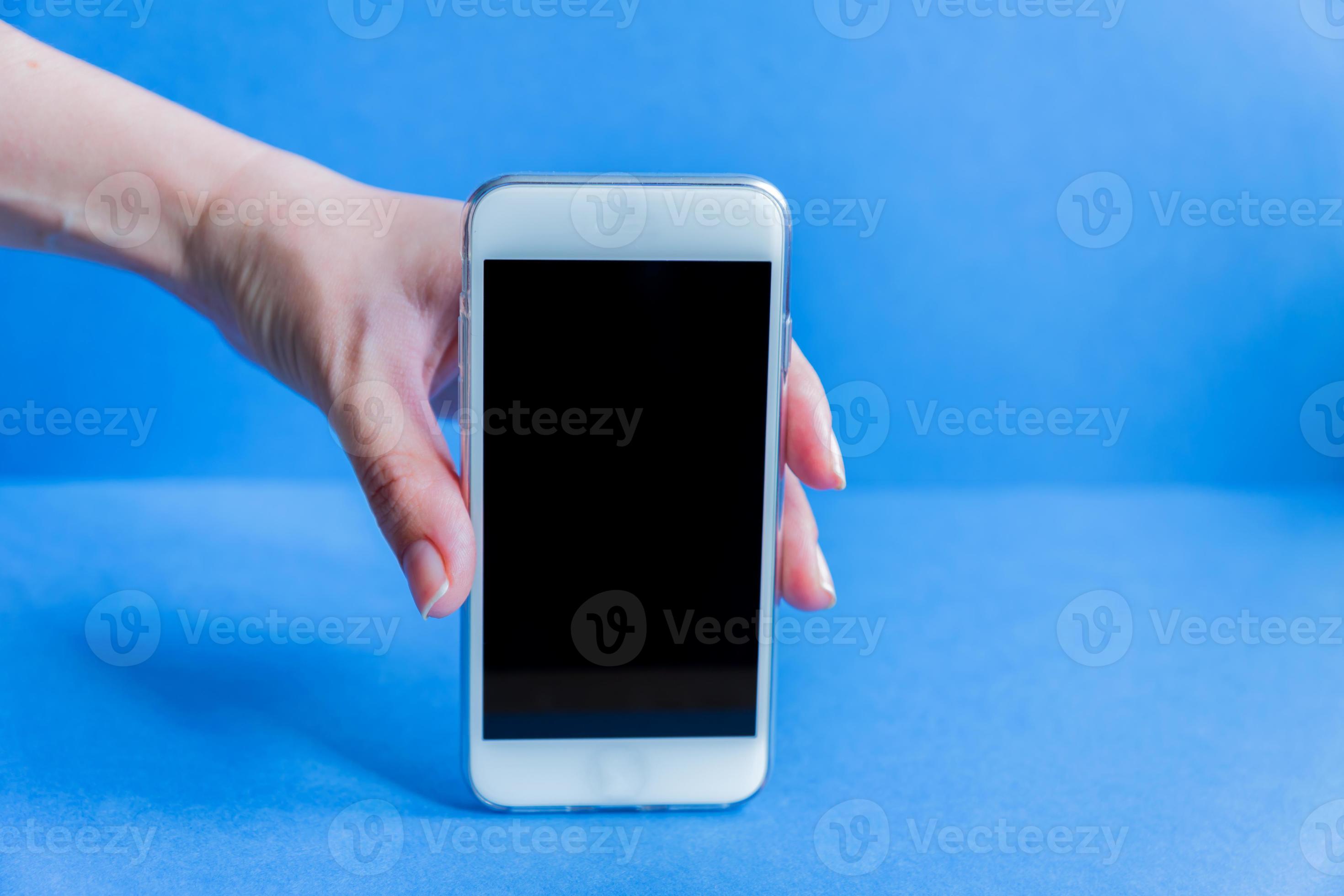 white mobile phone in left female's hand on blue background with copy