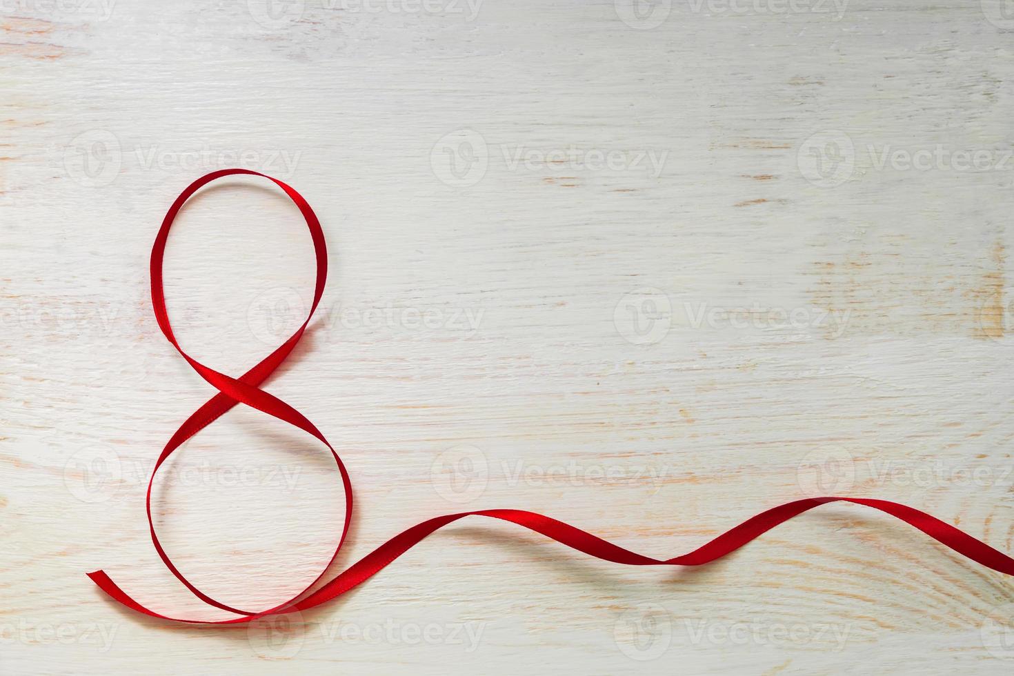 Red gift celebration ribbon waved in shape of number 8 on white wooden background. Greeting card with copy space for 8 March, International Women's Day photo