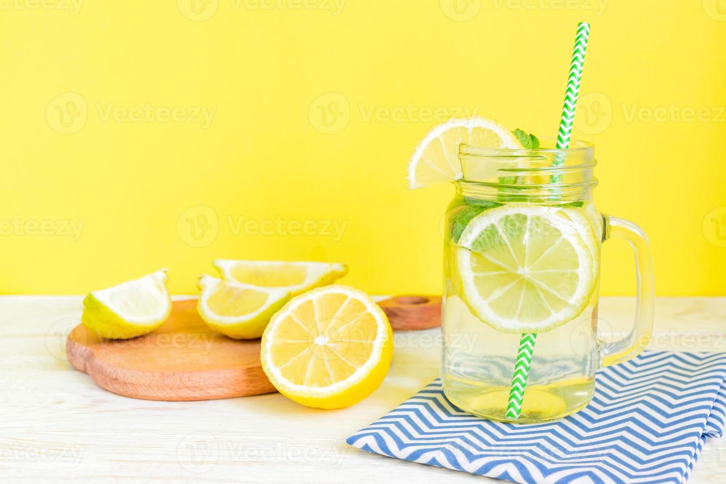 Citrus lemonade water with sliced lemon and mint, healthy and detox water drink in summer on wooden table with yellow background photo