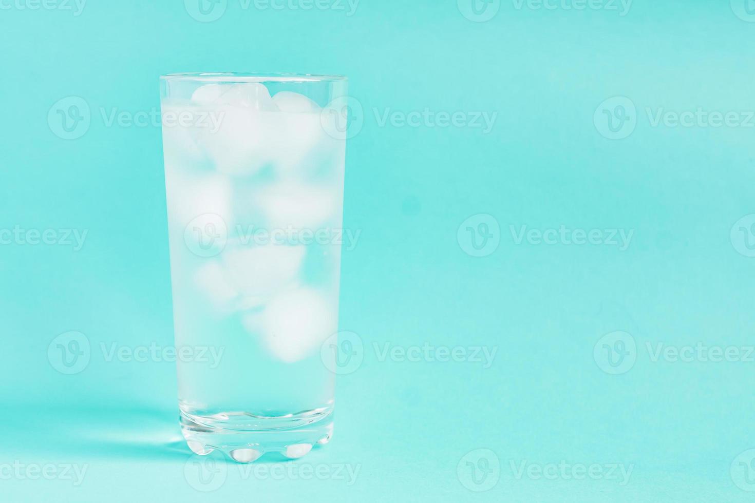 Close up of pure water with ice in tall transparent glass with copy space on blue background. photo