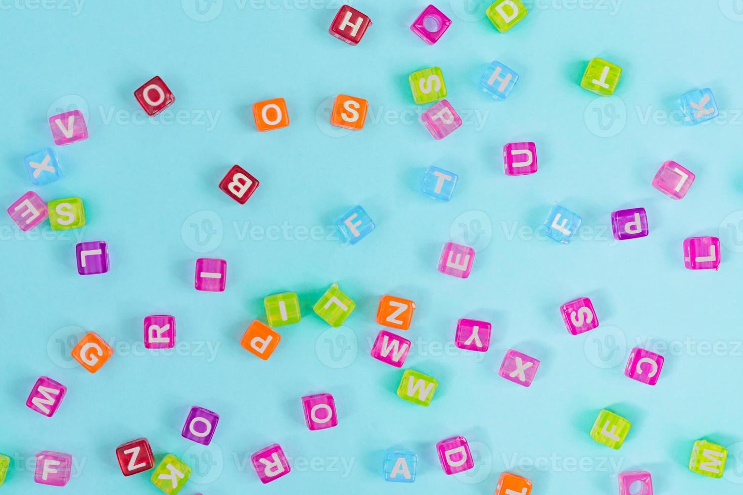 Multicolored plastic cube beads with letters scattered on blue background. Alphabet background texture. photo