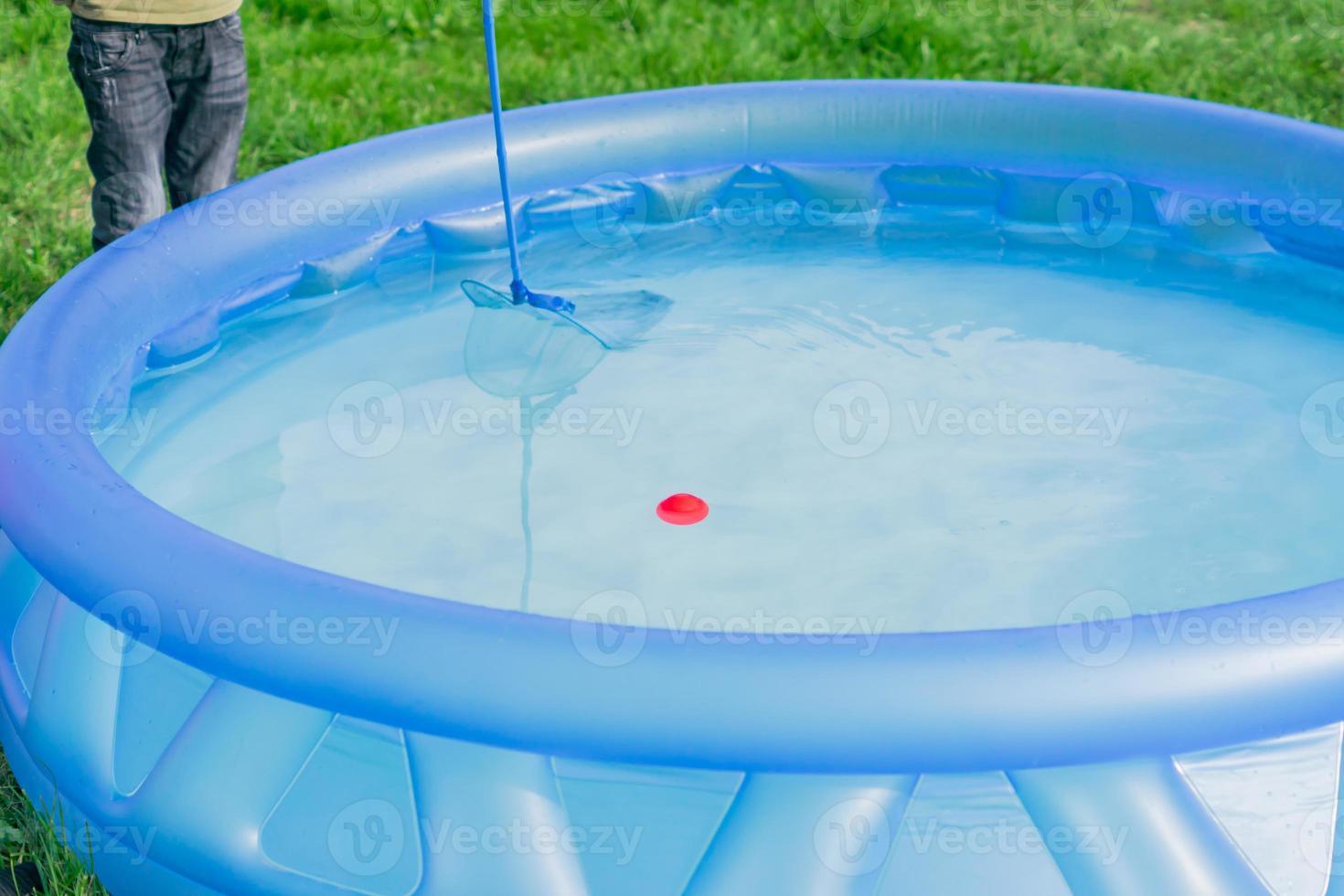 limpieza de piscina jardín. el chico intenta atrapar la bola roja con una red skimmer foto