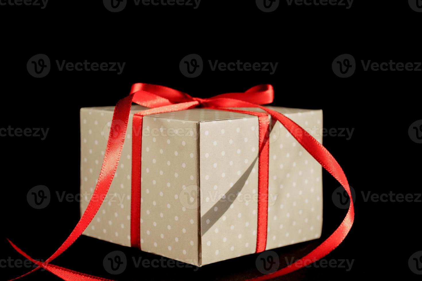 Beige polka dot gift box with red ribbon bow on black background with copy space. photo