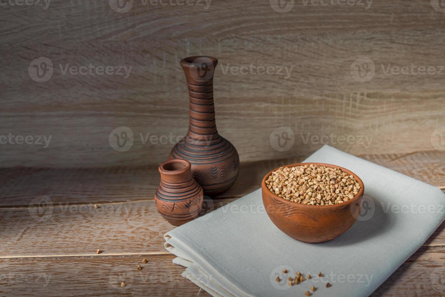 Dry buckwheat in brown clay bowl on wooden table. gluten free grain for healthy diet photo