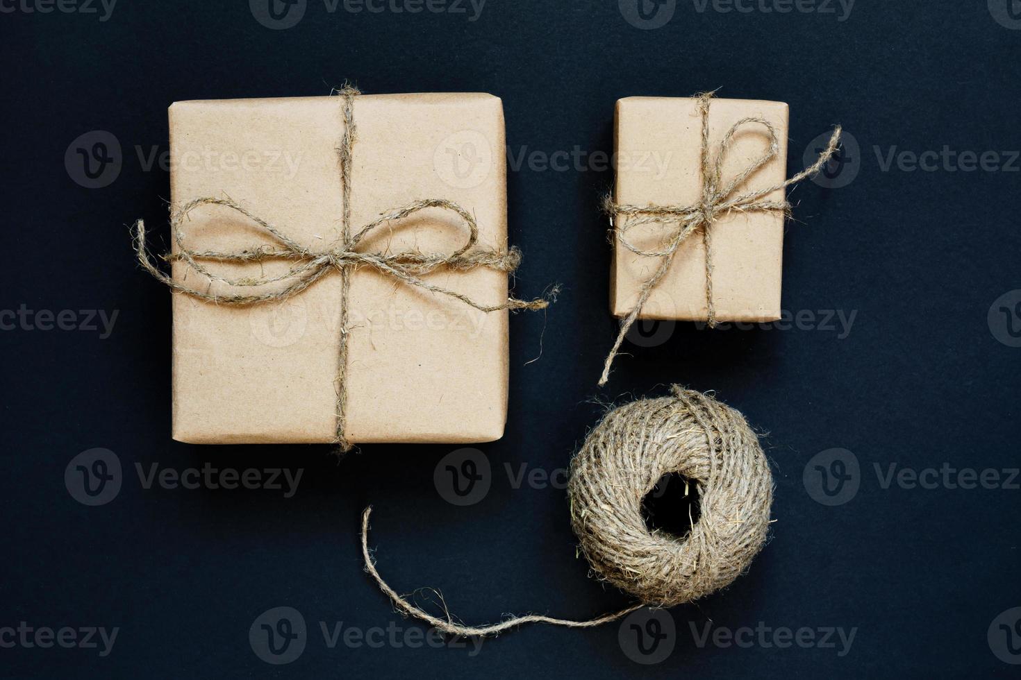 Handcrafted gift box wrapped in Craft paper with rope and bow on black background. Top view, flat lay photo