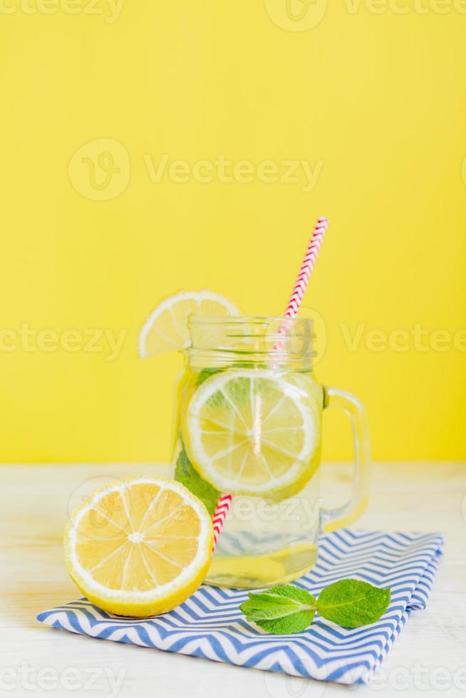 Citrus lemonade water with sliced lemon and mint, healthy and detox water drink in summer on yellow background. Summer bright backdrop with copy space photo