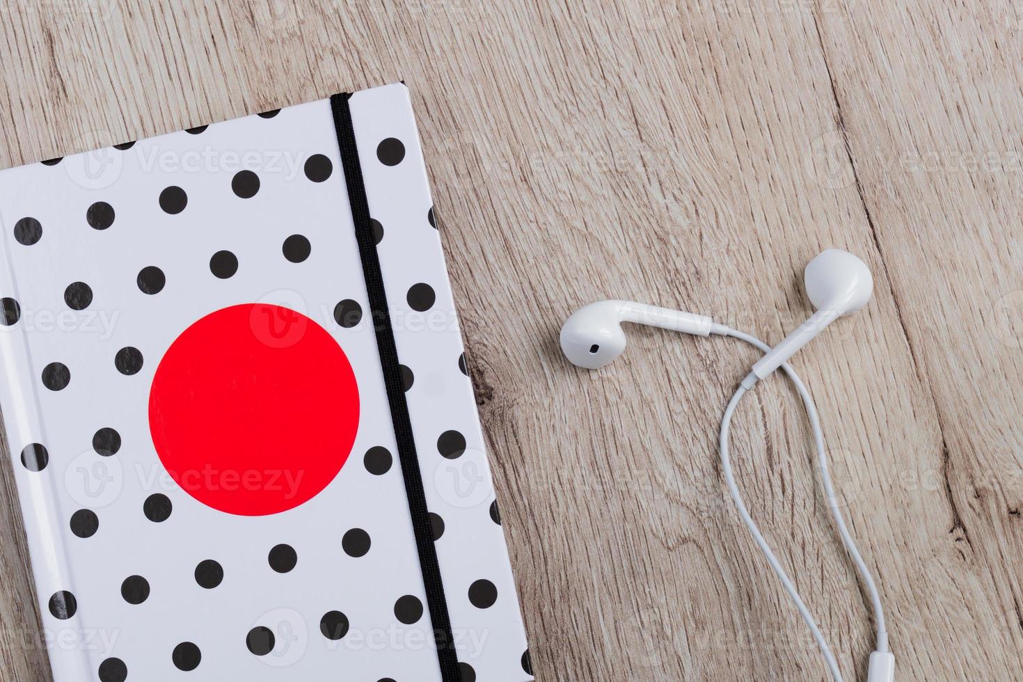 Top view of hotebook with polka dot cover and white headphones on wooden table. Minimal flat lay. photo