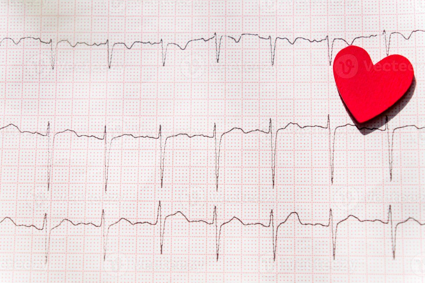 primer plano de un electrocardiograma en papel con corazón de madera roja. fondo de papel ecg o ekg. concepto médico y sanitario. foto