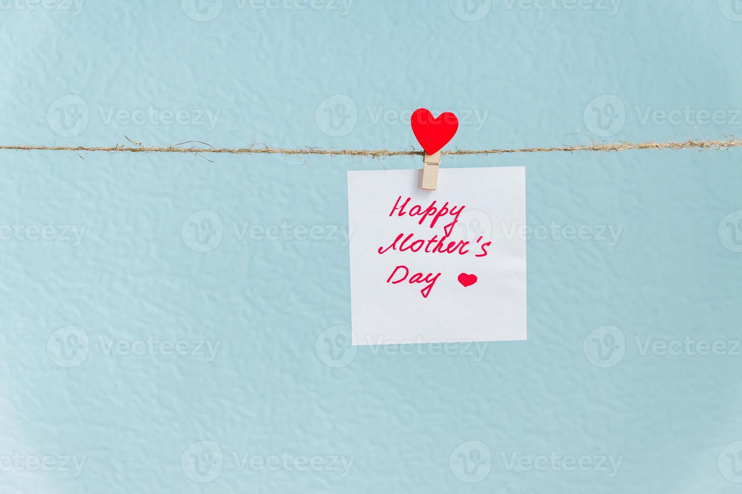 Pinned paper with happy mothers day inscription hanged on cord against blue background photo