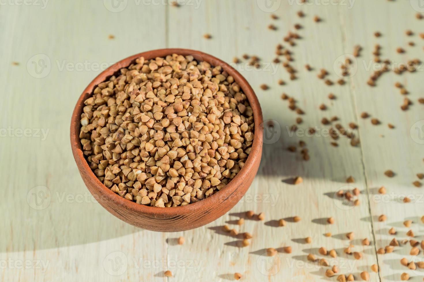 Dry buckwheat in brown clay bowl on wooden table. gluten free grain for healthy diet photo