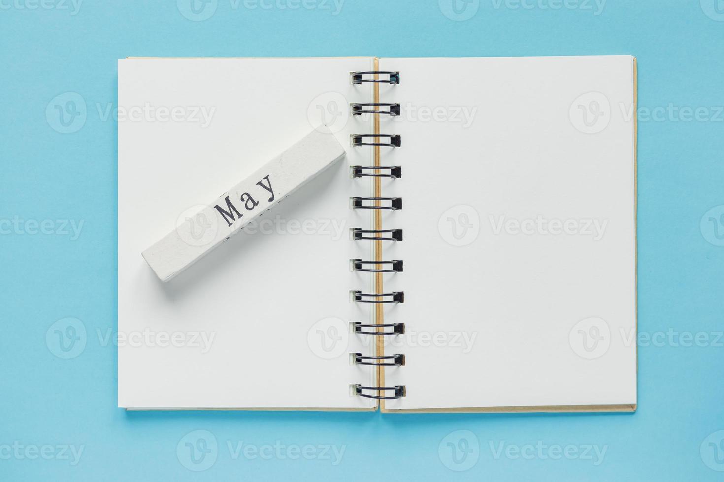 Clean spiral note book for notes and messages and may wooden calendar bar on blue background. Minimal business flat lay photo