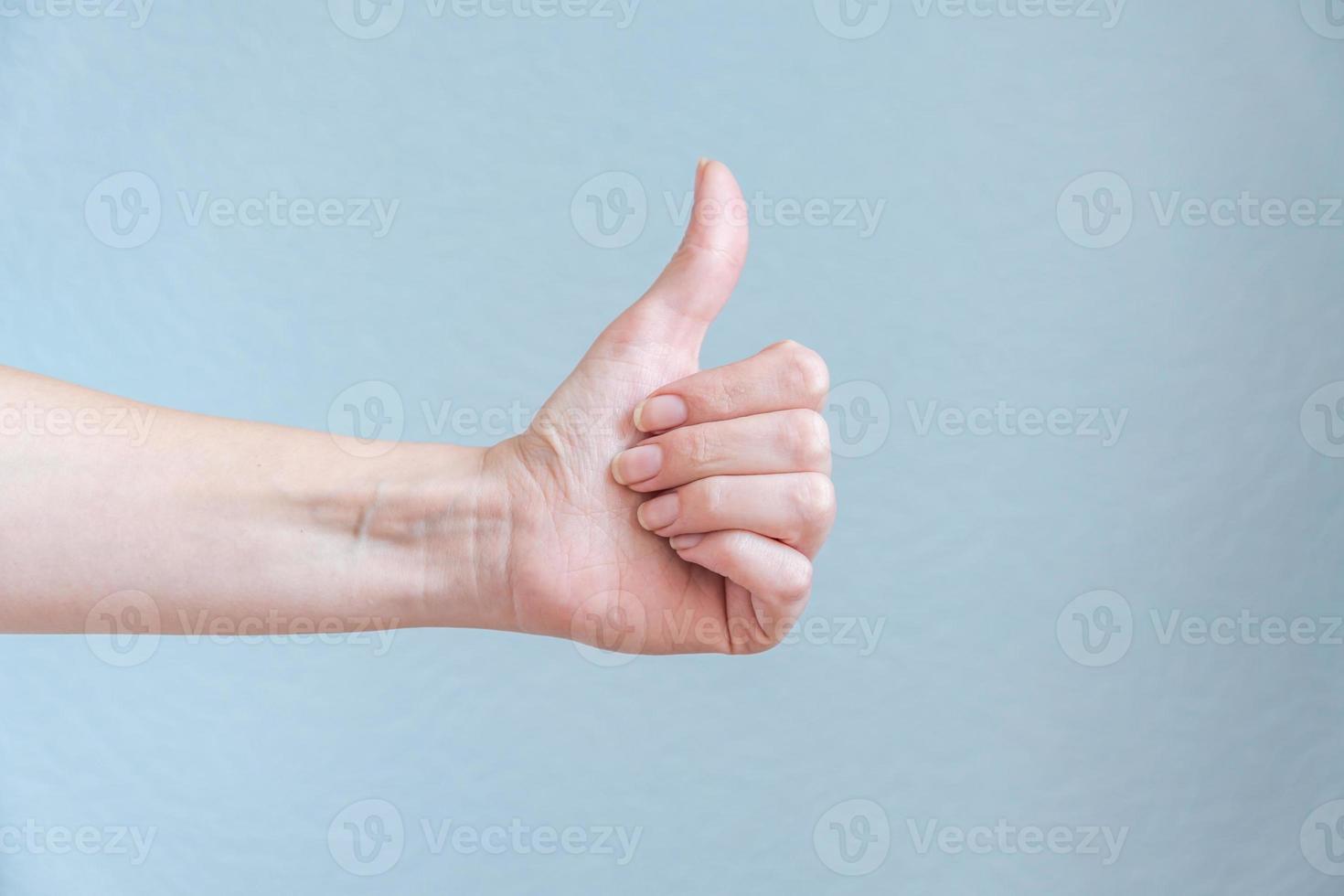 Female hand showing thumb up on blue background. Satisfaction concept. photo