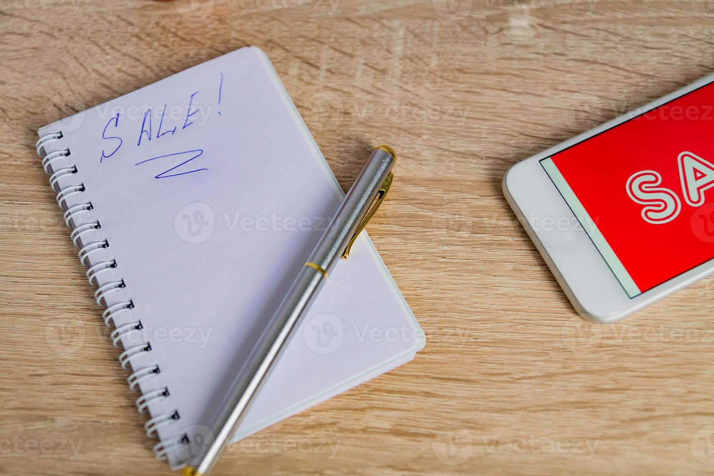 close up view of office desk with white smartphone with sale text, note and pen. Technology business online shopping concept photo