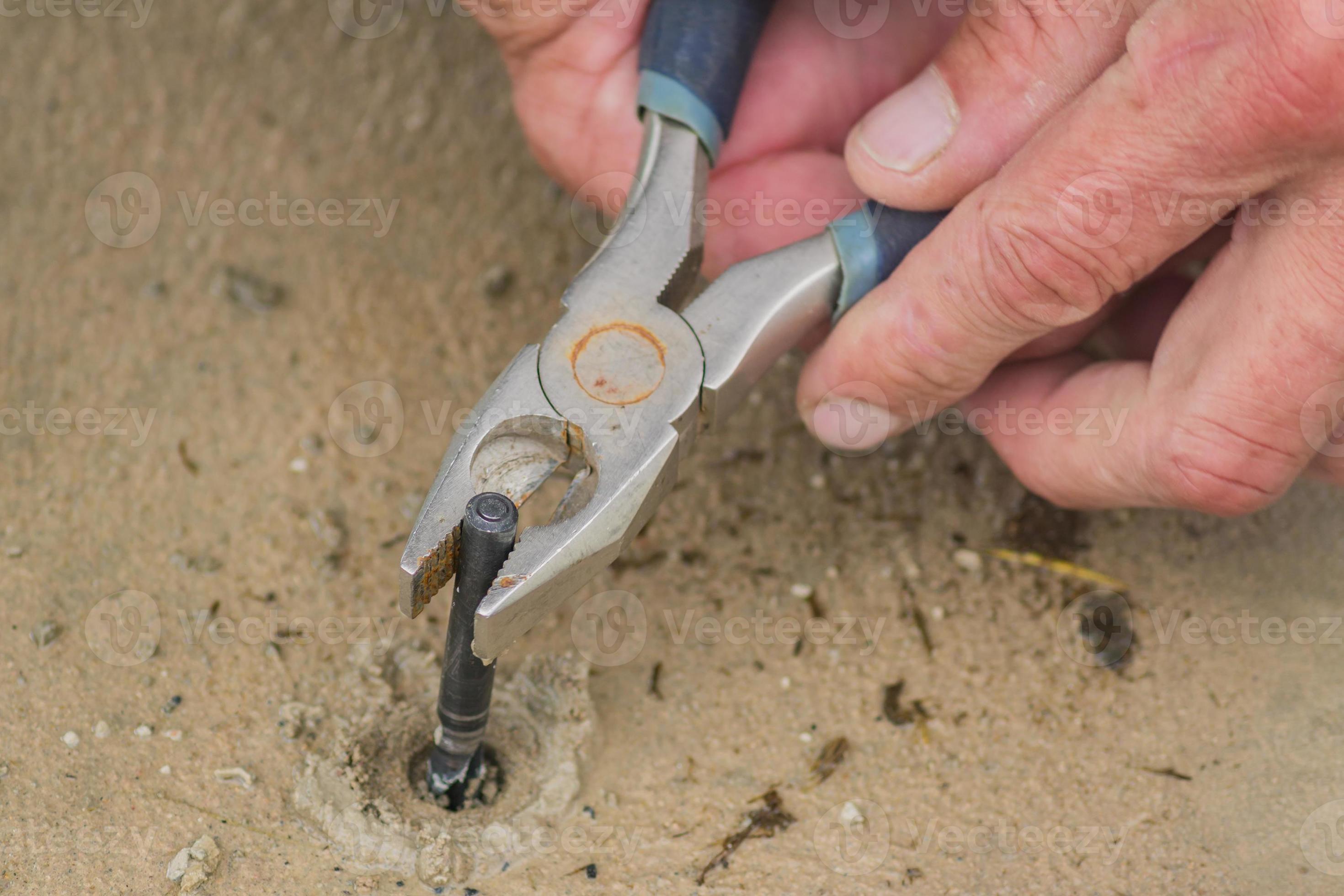 male hands pull out jammed drill bit whith pliers 10607599 Stock Photo