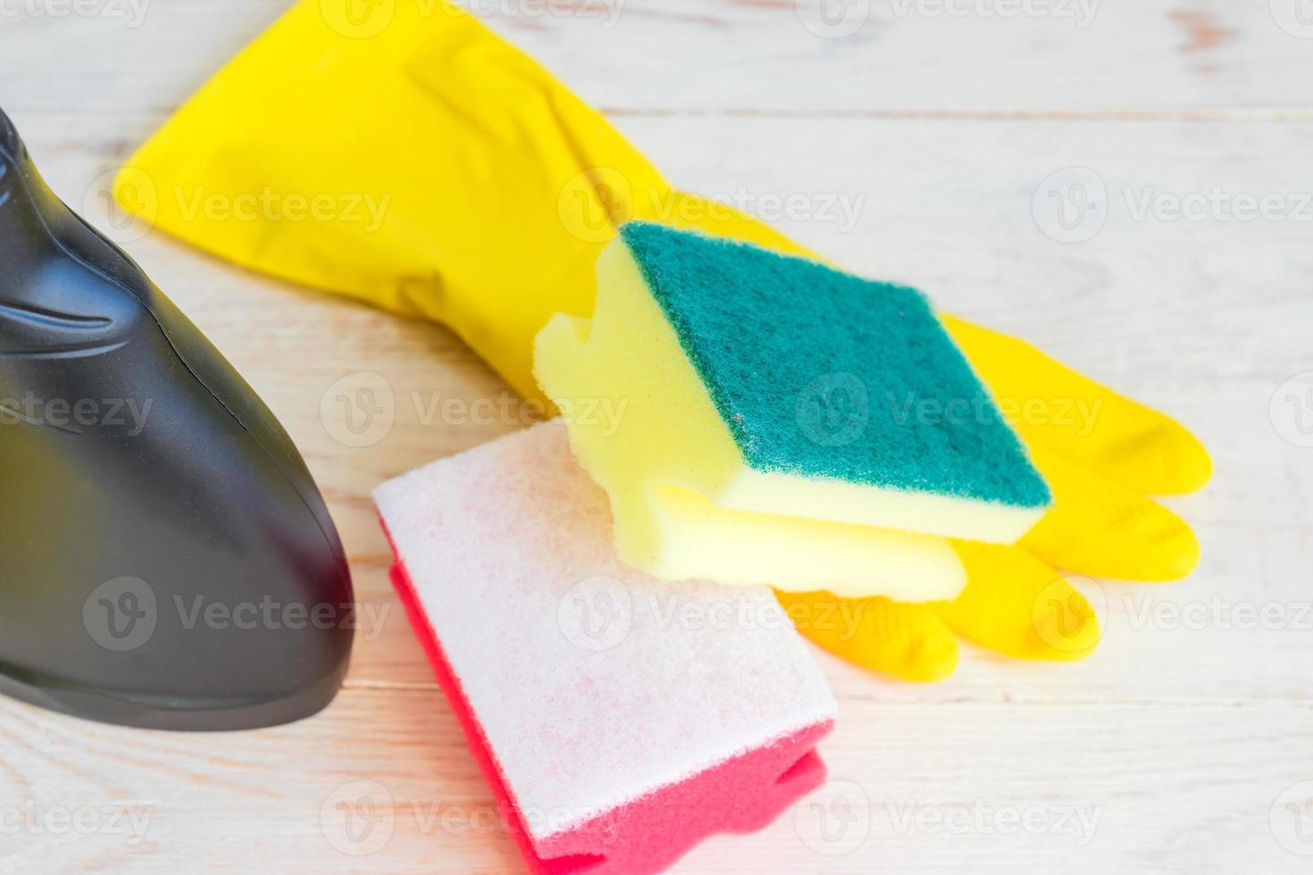 Close up of twoo clening sponges, yellow rubber gloves and black plastic spray bottle of detergent on wooden background. photo