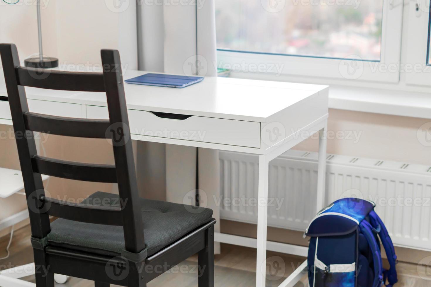 el lugar de trabajo del estudiante en casa. escritorio blanco y silla negra cerca de la ventana. foto