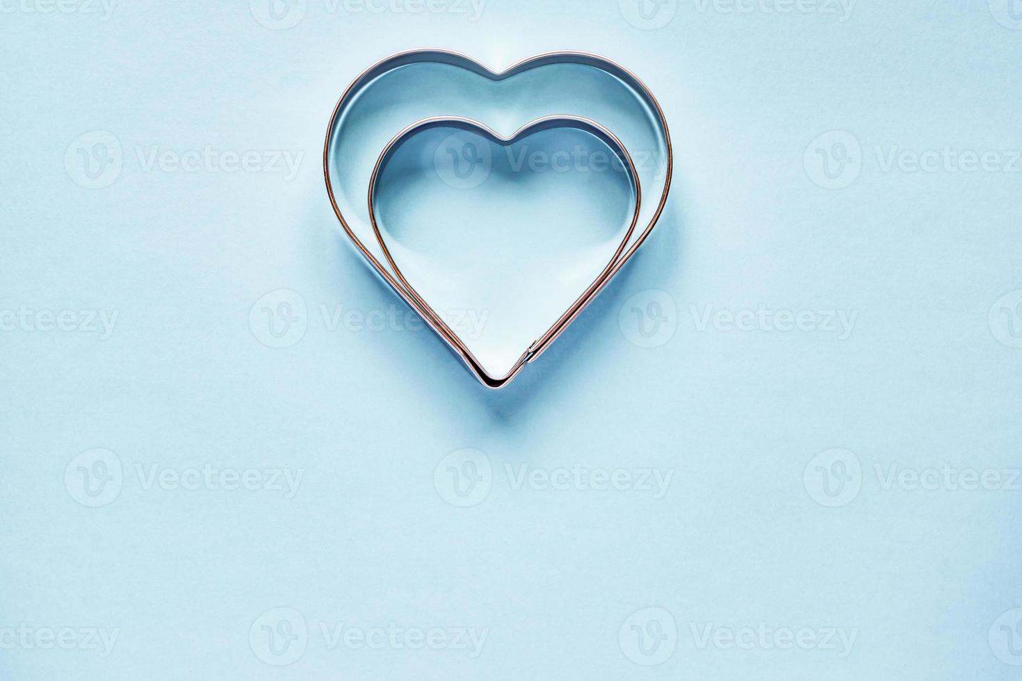 Two metal cookie cutters in heart shape on light blue background with copy space photo