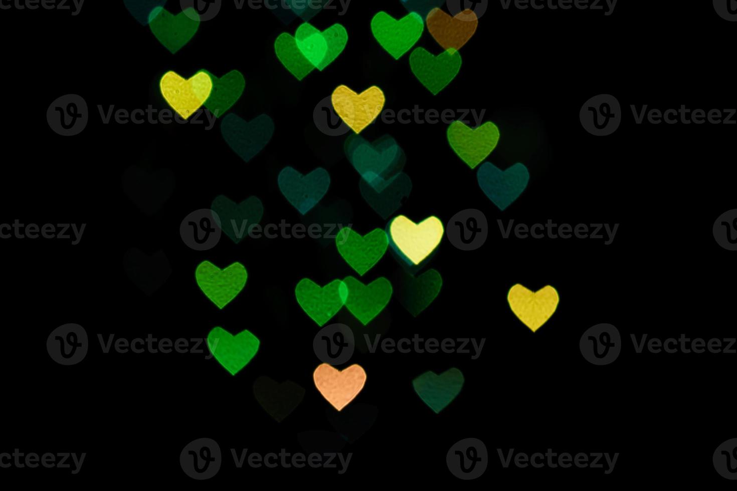 Multicolored hearts bokeh of green and yellow colores on black background. Texture for holidays photo