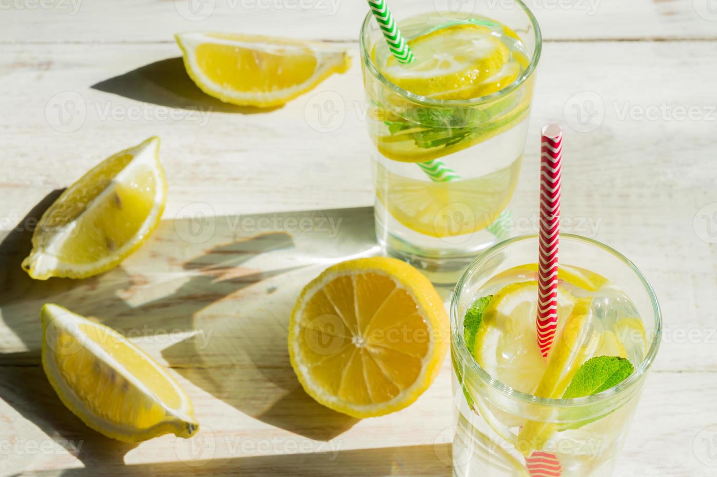 glass of homemade lemonade with lemons, mint and paper straws on wooden rustic background. Summer refreshing beverage. hard shadows photo