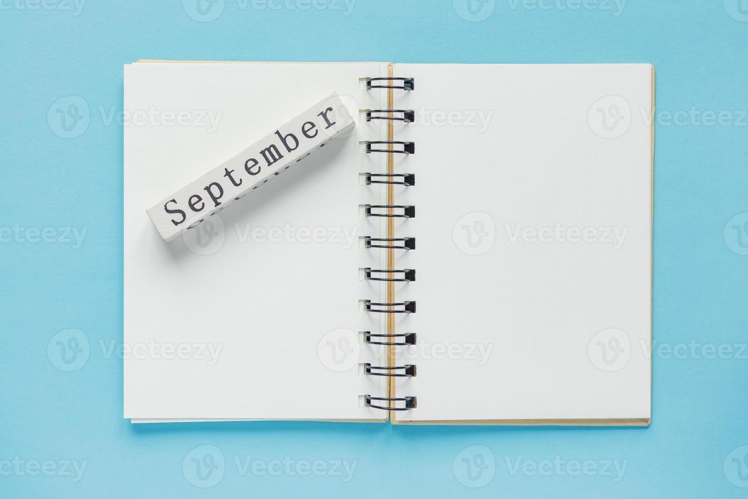 Clean spiral note book for notes and messages and september wooden calendar bar on blue background. Minimal business flat lay photo