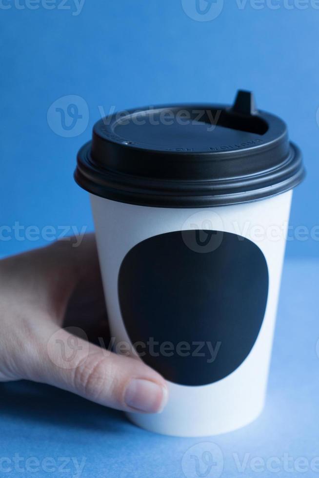 vaso desechable de papel kraft blanco para café con tapa de plástico negro. café para ir sobre fondo azul. foto