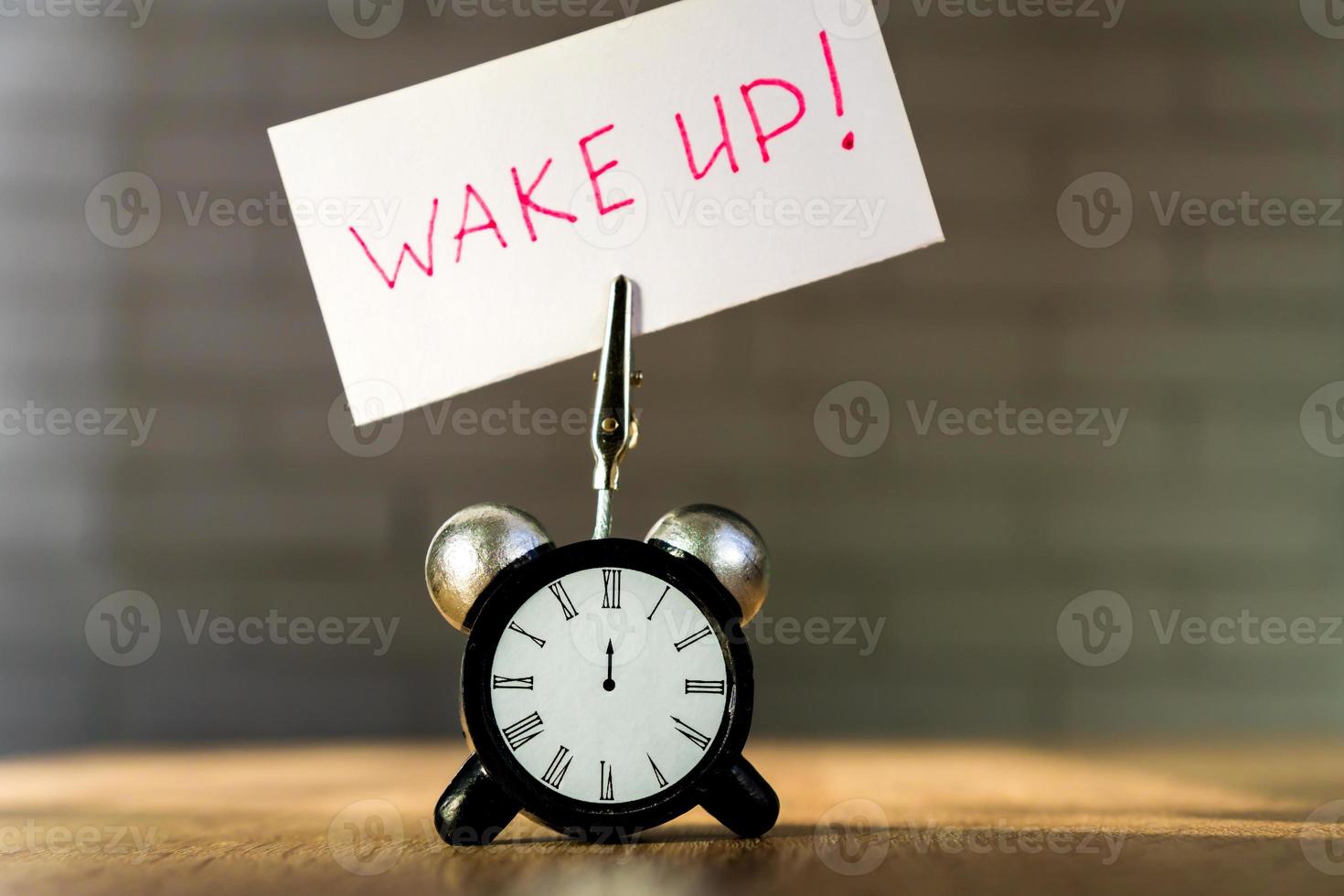 Alarm clock and banner with handwritten phrase wake up on wooden table. Time management concept. photo