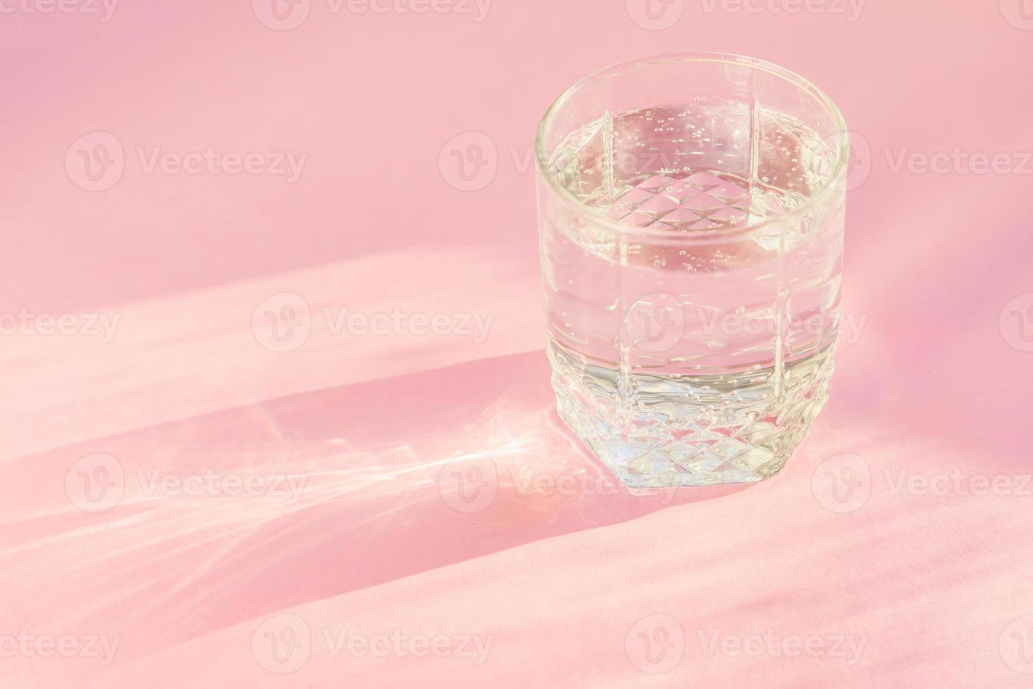 Close up of sparkling water in transparent glass and sun glare on pink background. photo