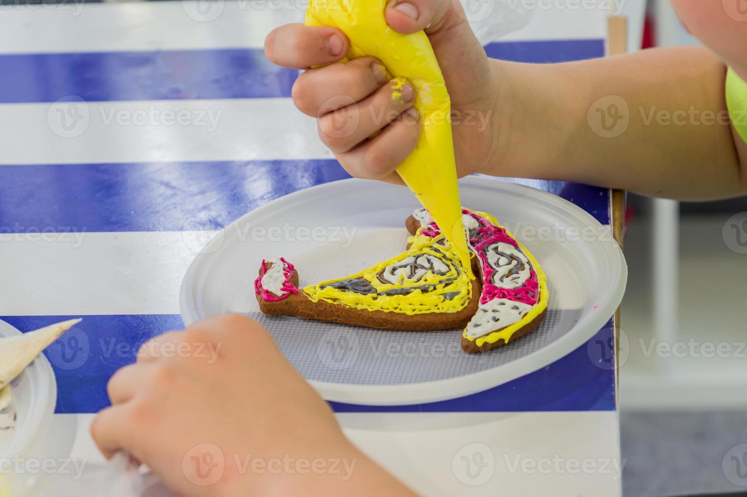 Toddler boy decorates ginger bread in shape of boat with glase. Street workshop at the festival photo