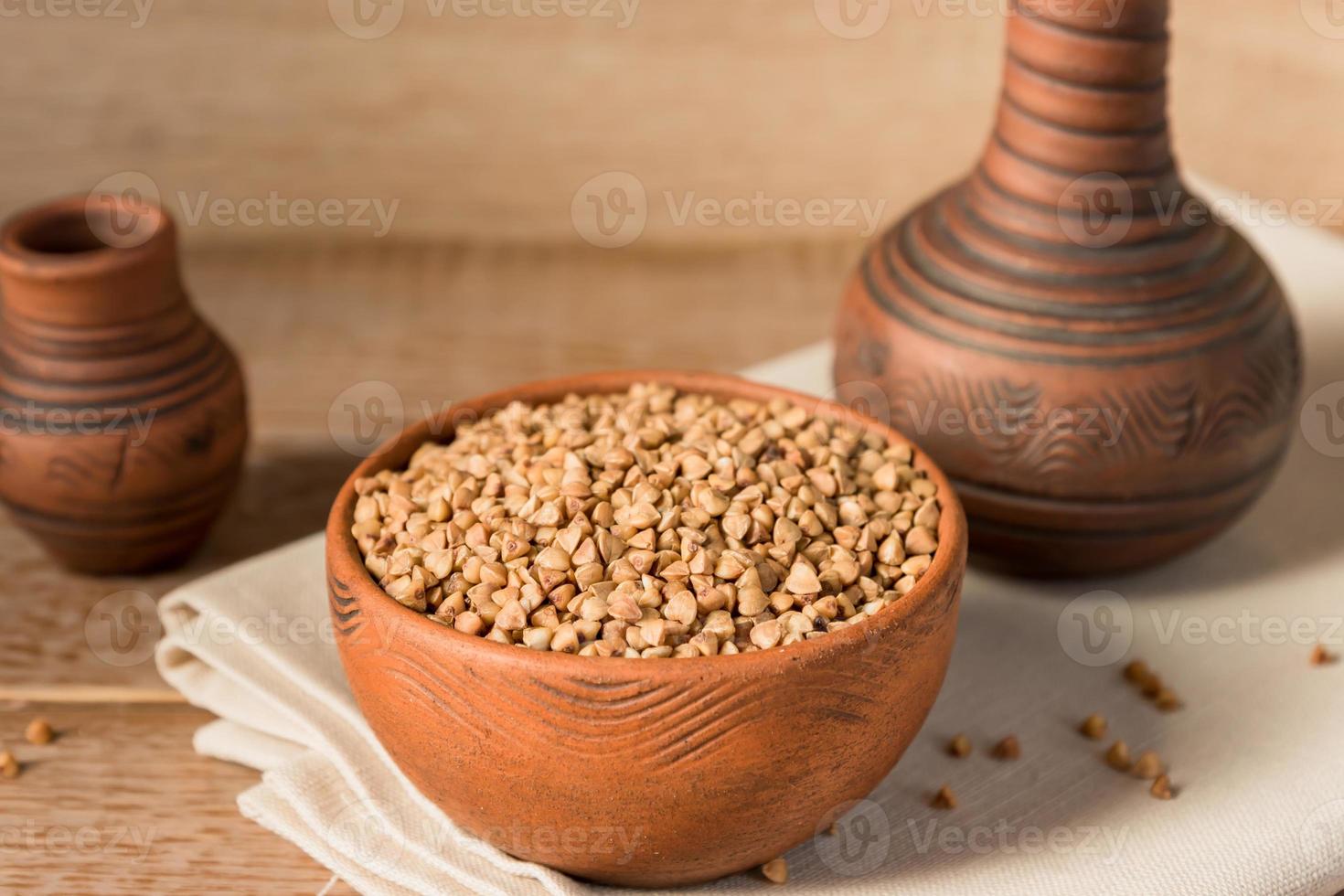 Dry buckwheat in brown clay bowl on wooden table. gluten free grain for healthy diet photo