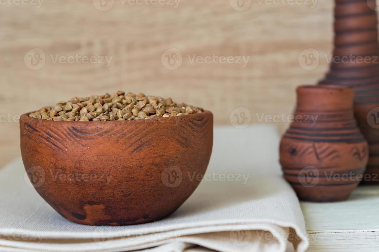 Dry buckwheat in brown clay bowl on wooden table. gluten free grain for healthy diet photo