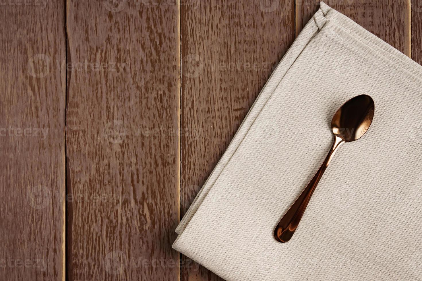 Top view of cloth napkin of beige color and served tea spoon on wooden table. photo