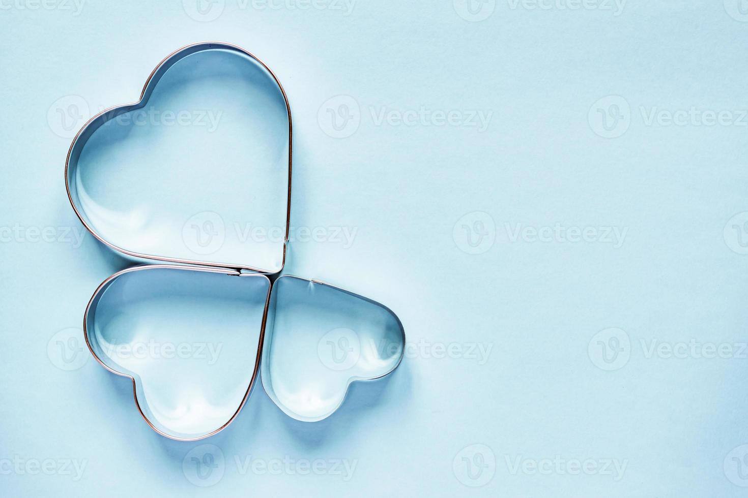 Three metal cookie cutters in heart shape on light blue background with copy space photo
