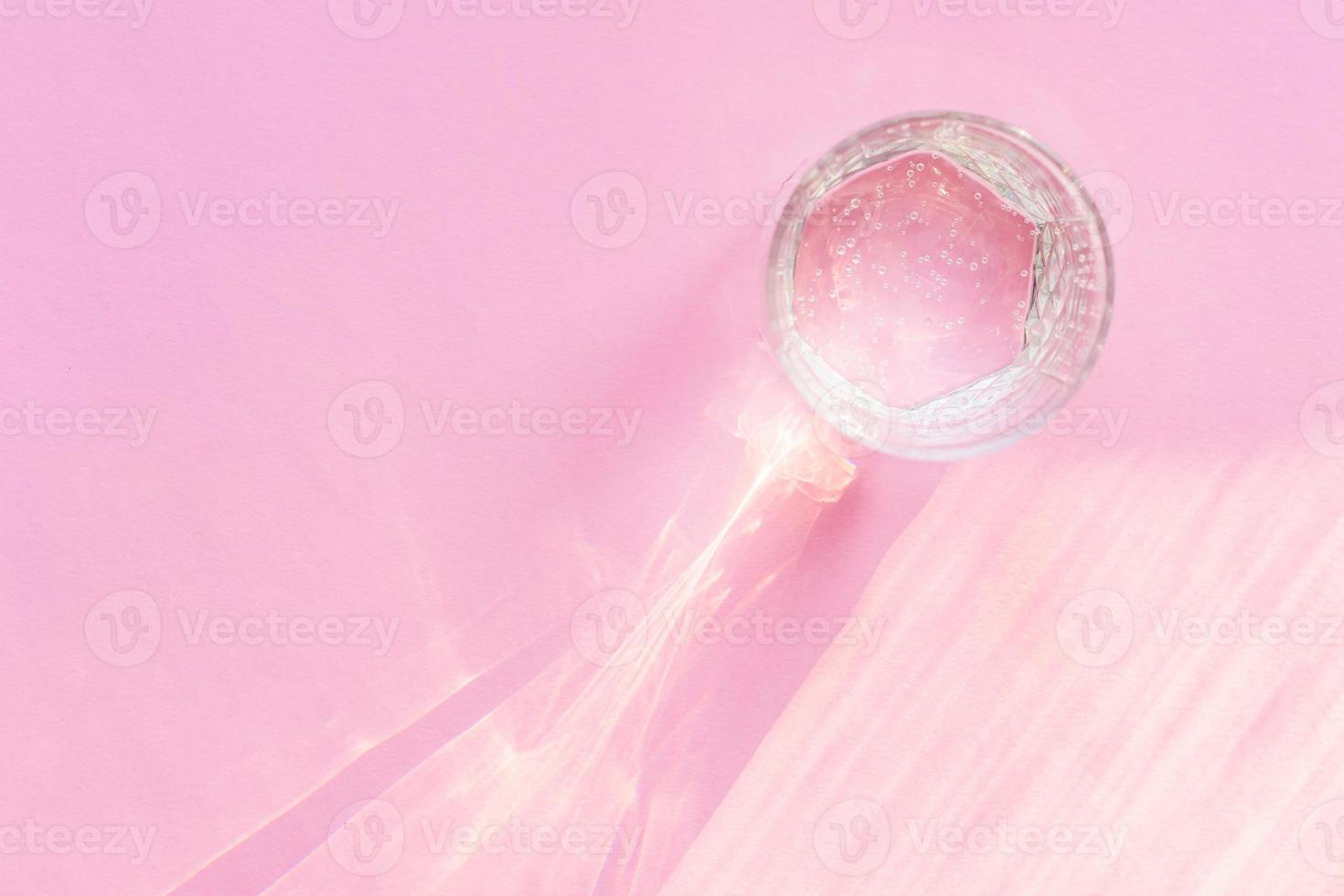 Top view of sparkling water in transparent glass and sun glare on pink background. photo