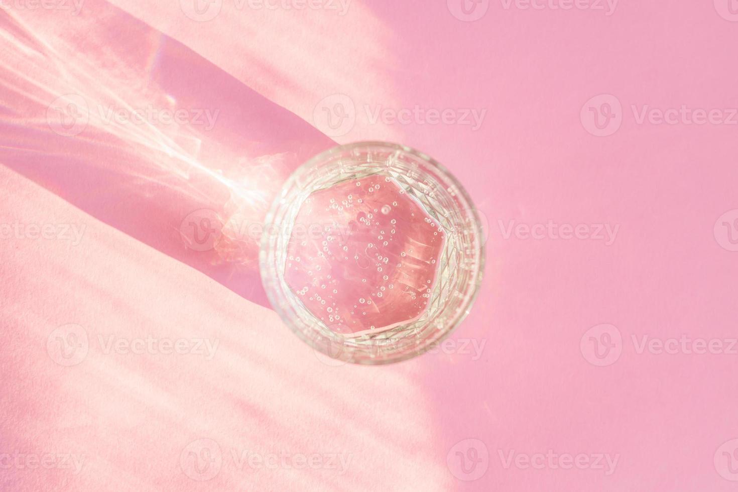 Close up of sparkling water in transparent glass and sun glare on pink background. photo