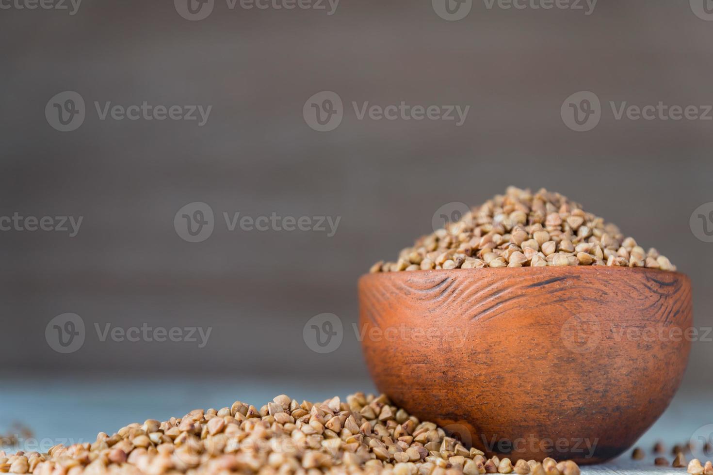 Dry buckwheat in brown clay bowl on wooden table. gluten free grain for healthy diet photo