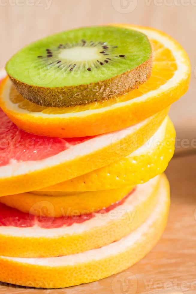 stack of slice of oranges, lemons, kiwi, grapefruit on wooden background photo