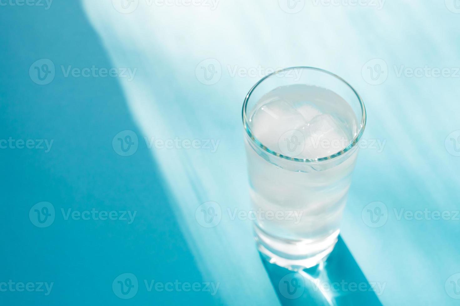 Close up of pure water with ice and paper straw in transparent glass and sun glare on blue background. photo
