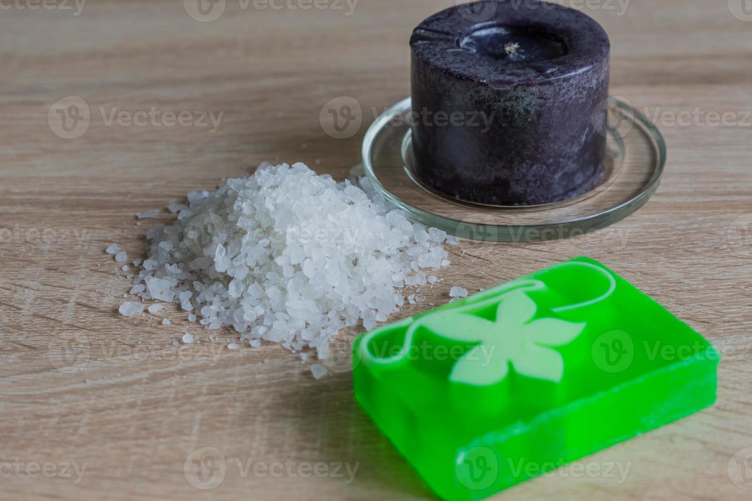 Pile of sea salt, soap bar and black candle on wooden table. Natural ingredient for spa and exfoliation. photo