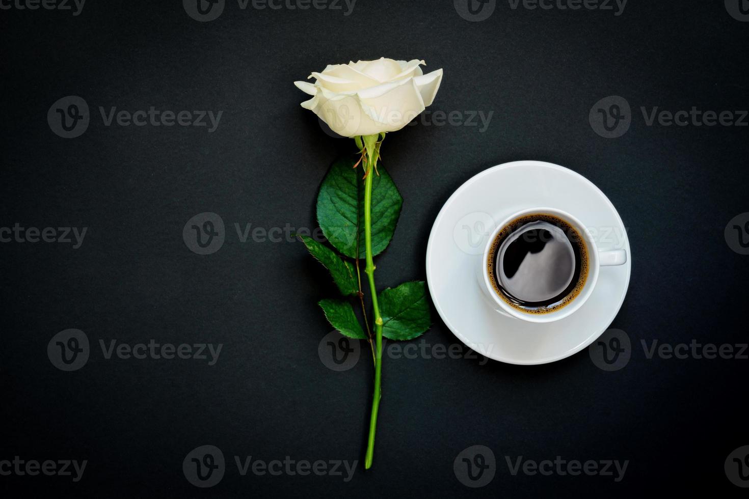 Cup of black coffee and white rose on black background, Top view, copy space. photo