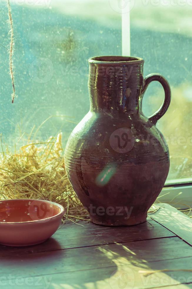 Old clay ceramic jar and clay bowl on wooden table near the window. Rustic still life. photo