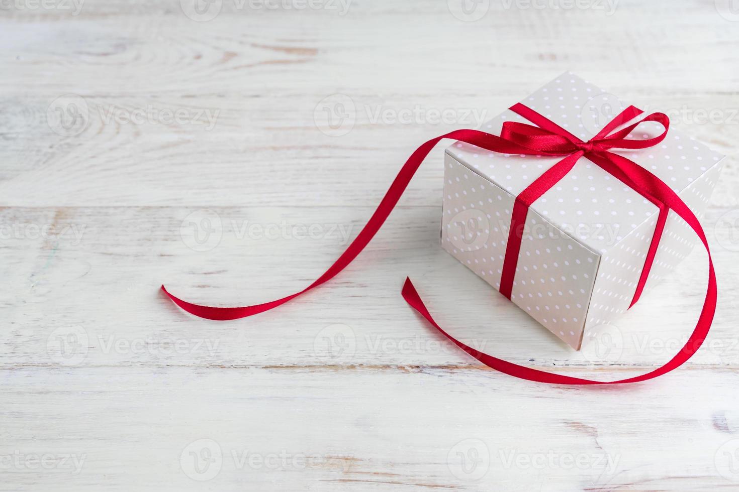 Beige polka dot gift box with red ribbon bow on wooden background with copy space. photo