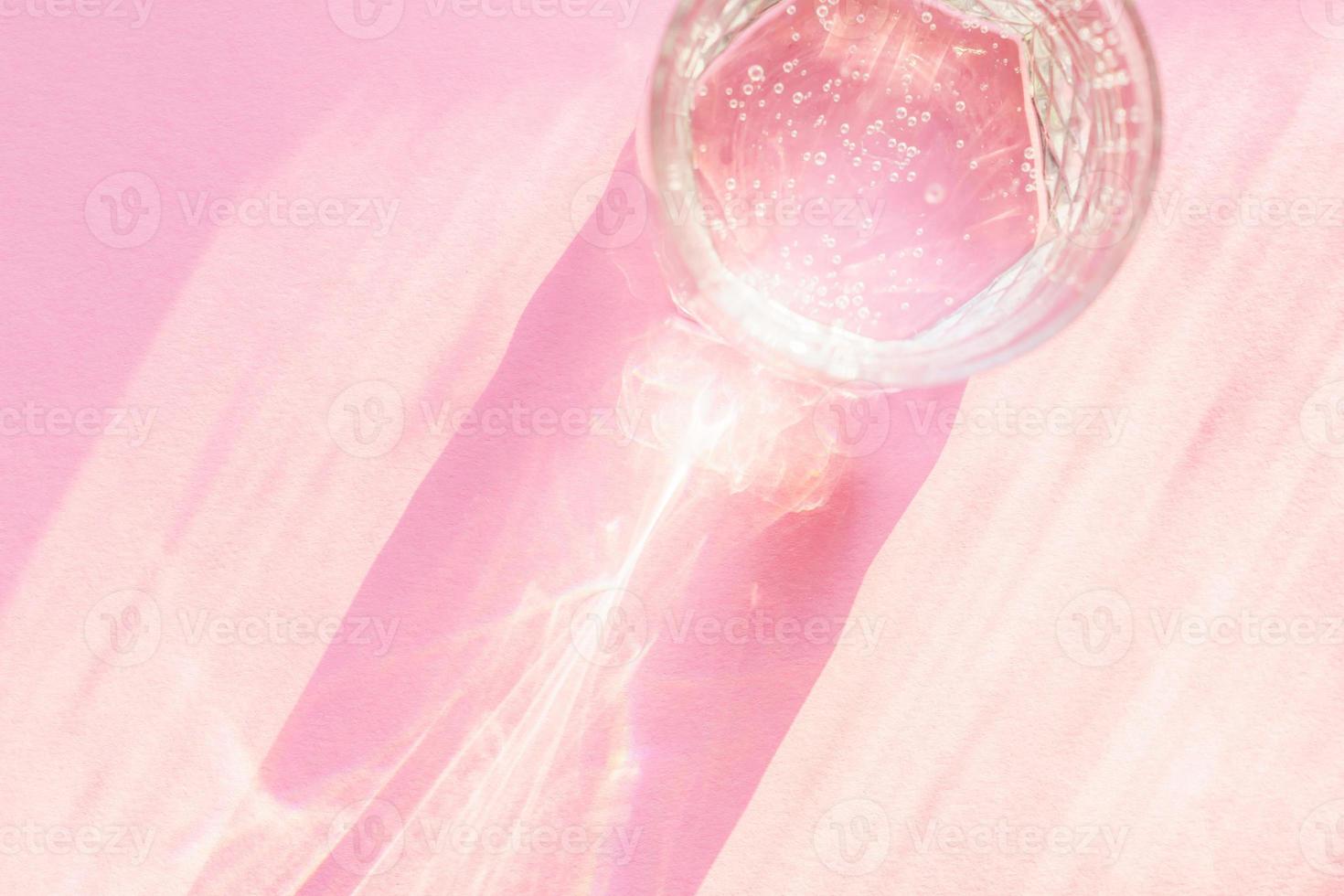 Top view of sparkling water in transparent glass and sun glare on pink background. photo