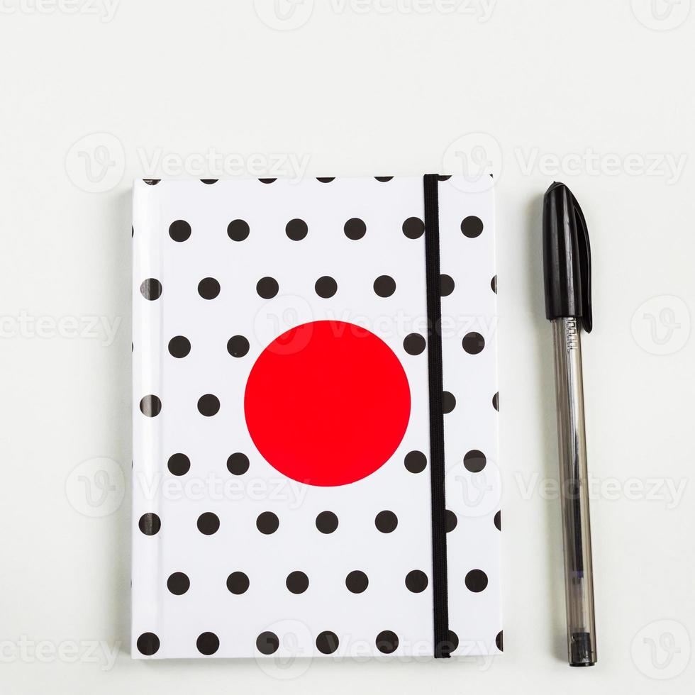 Black and white polka dot note book with red circle  on the cover and black pen on white table. top view, minimal flat lay photo