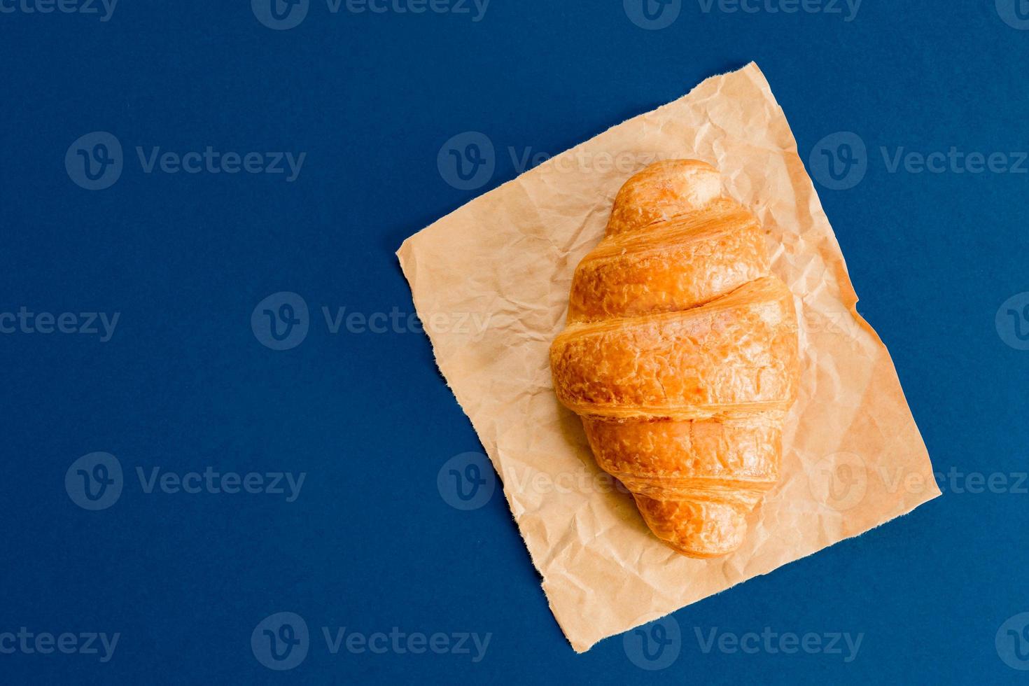 top view of croissant on craft paper on blue background with copy space. photo
